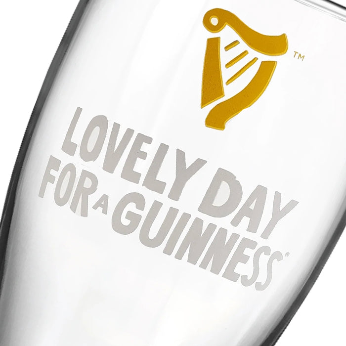 A Guinness Summer Collection Lovely Day Pint Glass featuring a gold harp logo and the grey text “Lovely Day for a Guinness.”
