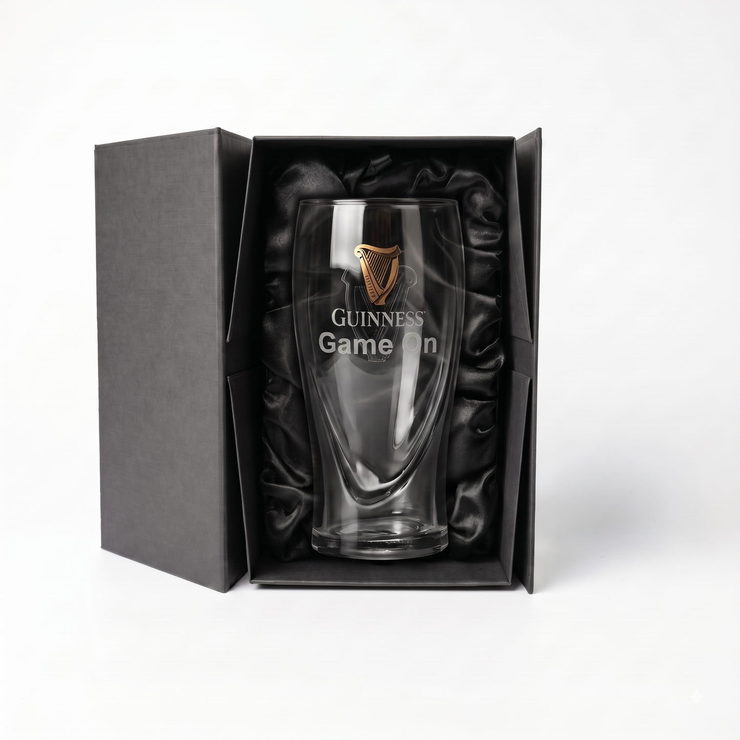 Showcased in an open luxury gift box lined with black satin, the Guinness Webstore US Guinness Pint Glass Luxury Gift Box features a clear pint glass adorned with a gold Guinness logo and “Game On” text, making for an impressive presentation.