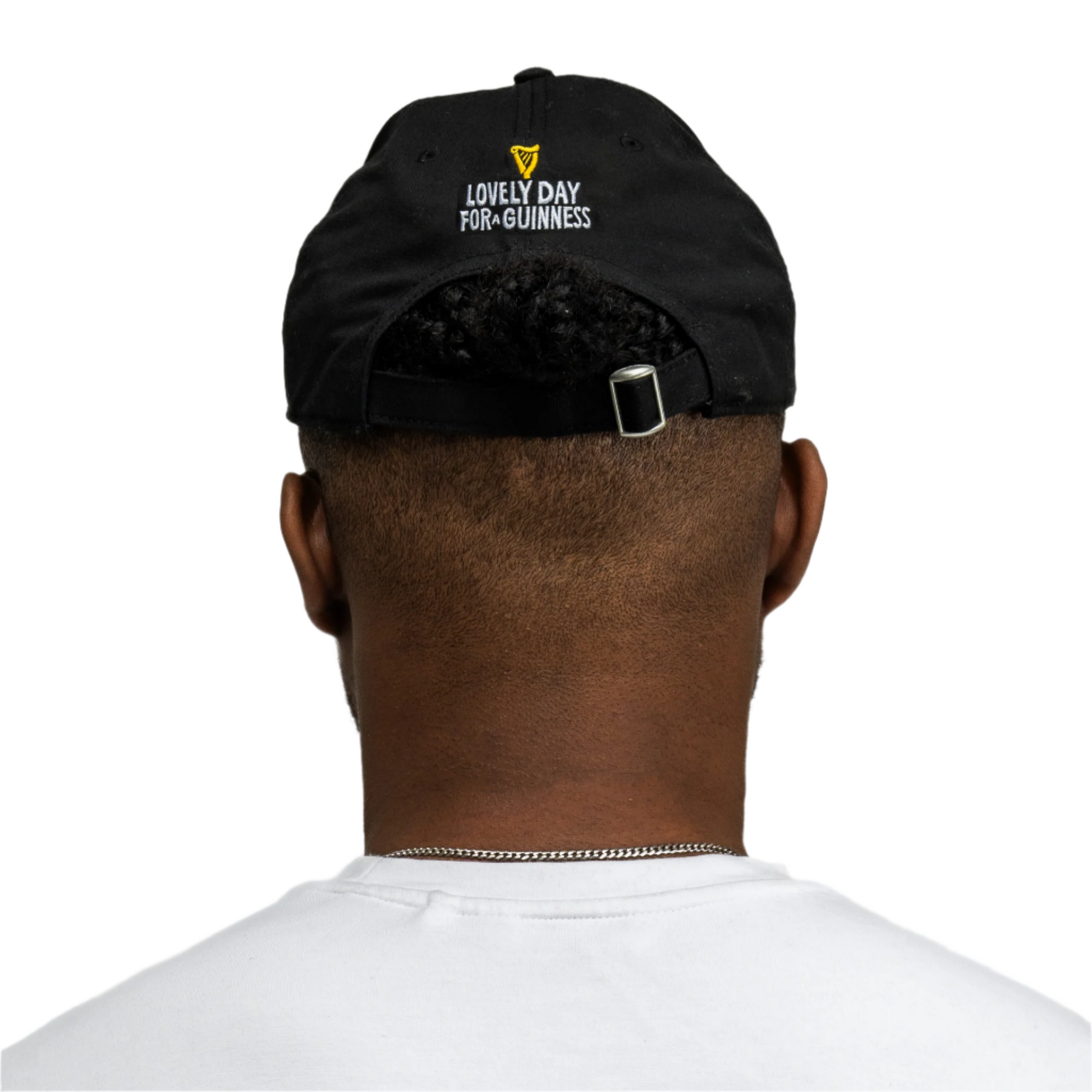 A person is seen from behind wearing the black Guinness Seb Curi Lovely Day Cap from Guinness Webstore US, featuring the classic slogan, paired with a white shirt against a plain background.