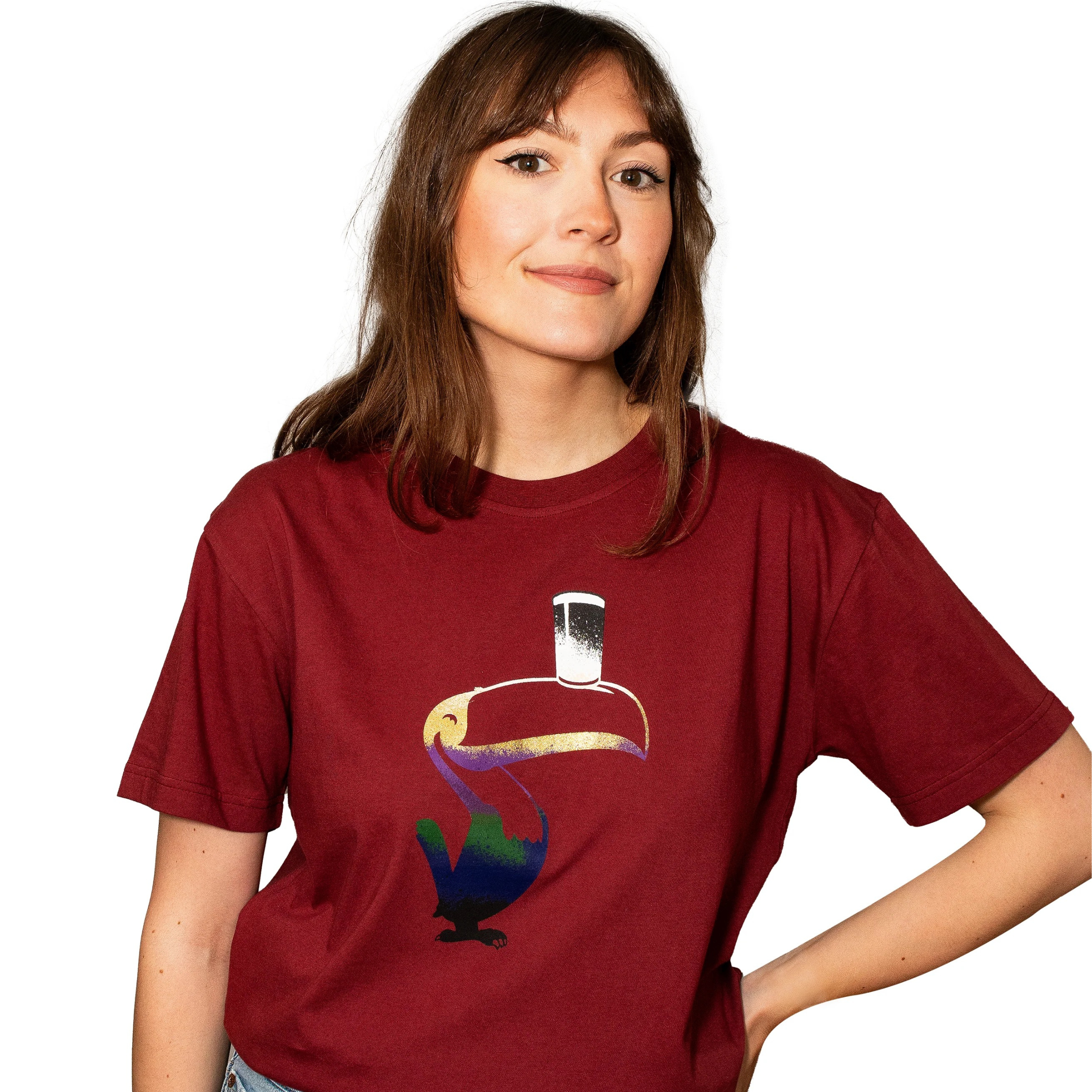 A woman wears the Guinness Liquid Toucan Tee - Red by Guinness, featuring a stylized toucan with a pint glass on its beak, standing against a white background.