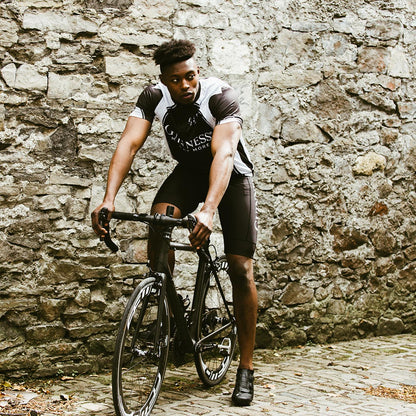 A man wearing a Guinness Performance Cycling Jersey, riding a bike in front of a stone wall with exceptional performance.