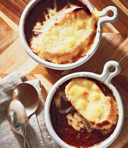 Two bowls of french onion soup on a wooden table, perfect for your Guinness Hardcover Cookbook.