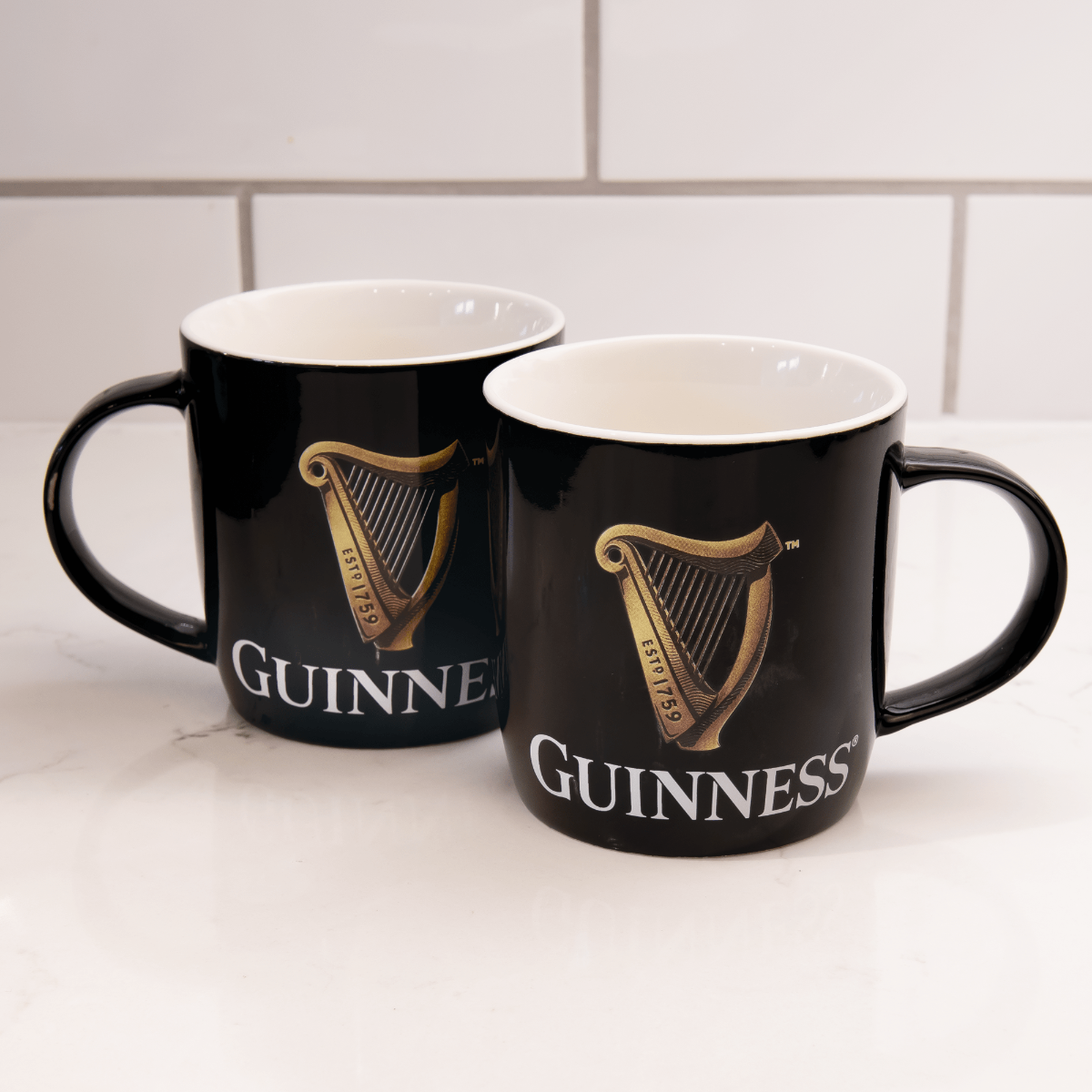 A Guinness Toucan Mug Set featuring two mugs adorned with a Toucan design displayed on a counter.