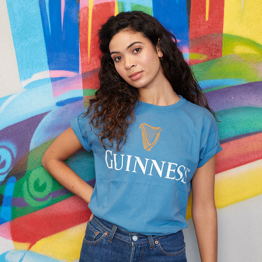A woman wearing a Guinness Trademark Label T-Shirt Blue standing in front of a colorful wall.