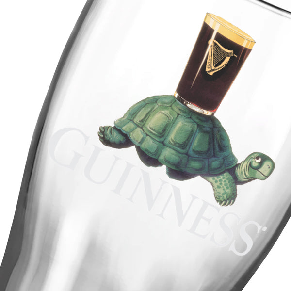 The Guinness Webstore US Guinness Gilroy Tortoise Pint Glass - 2 Pack features the classic Gilroy tortoise carrying a partially visible “GUINNESS” pint glass on its shell.