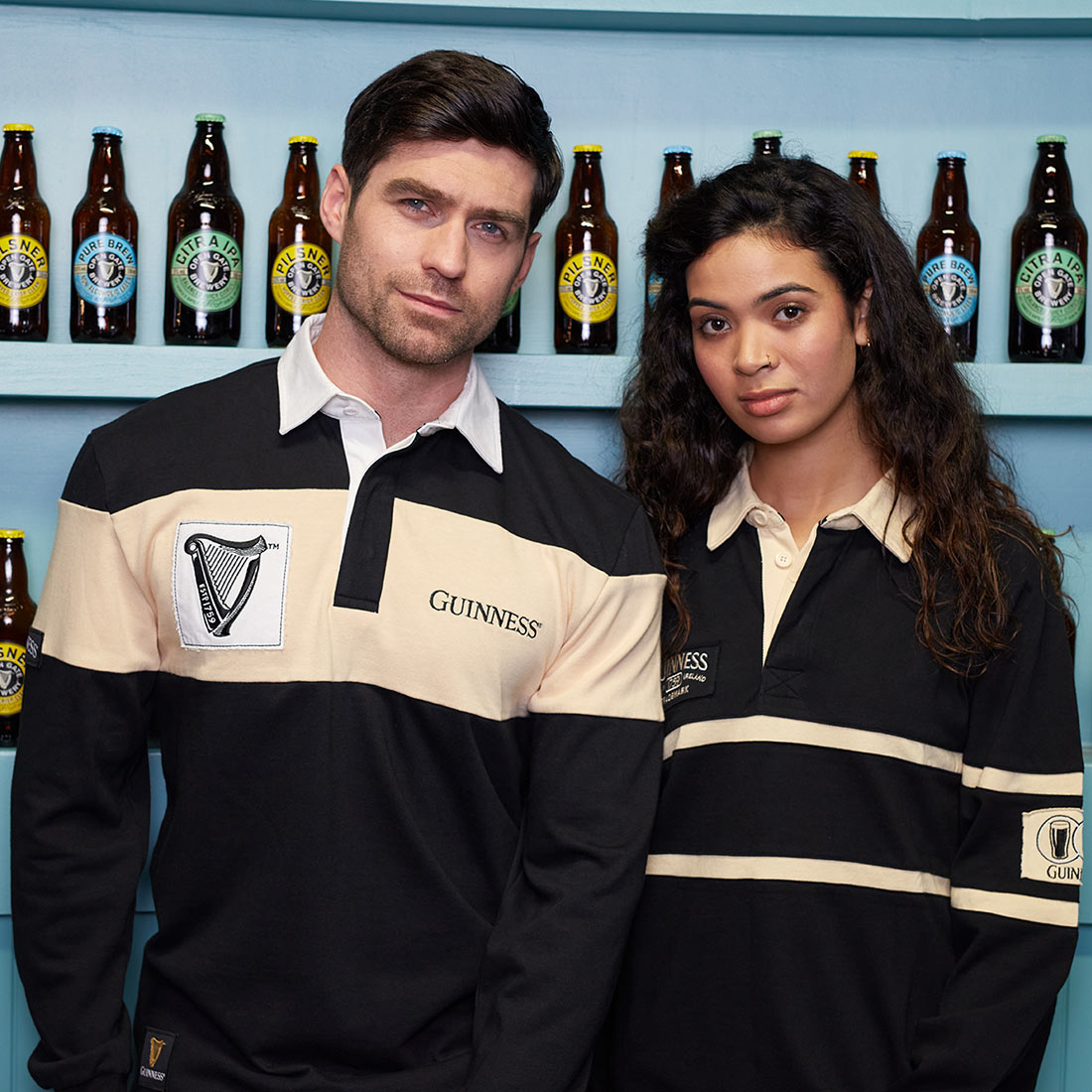 A man and a woman posing for a photo in a classic Guinness Traditional Rugby Jersey with Cream panel and Harp logo patch.