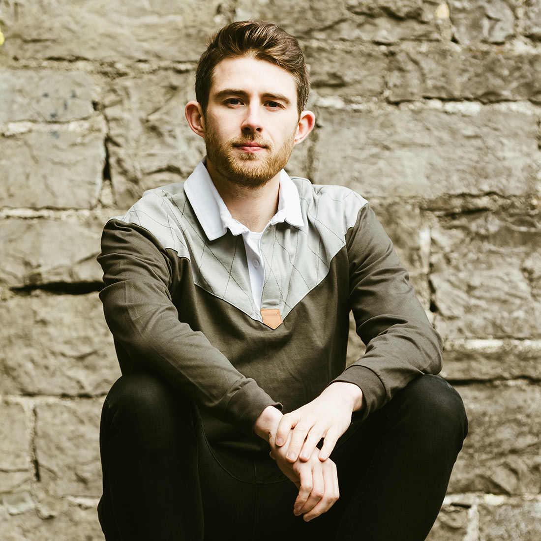 A man sitting on a bench with a skateboard, wearing the Guinness Heritage Charcoal Grey & Black Long-Sleeve Rugby made of cotton fabric.