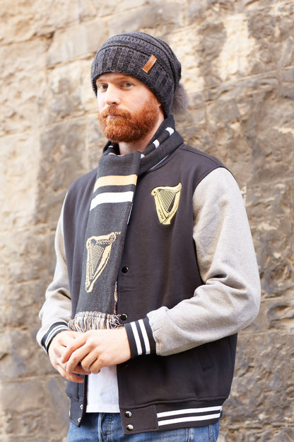 A man wearing a Guinness Dark Grey Slouchy Bauble Beanie with Brown Leather Patch and a scarf to stay warm during the winter months.