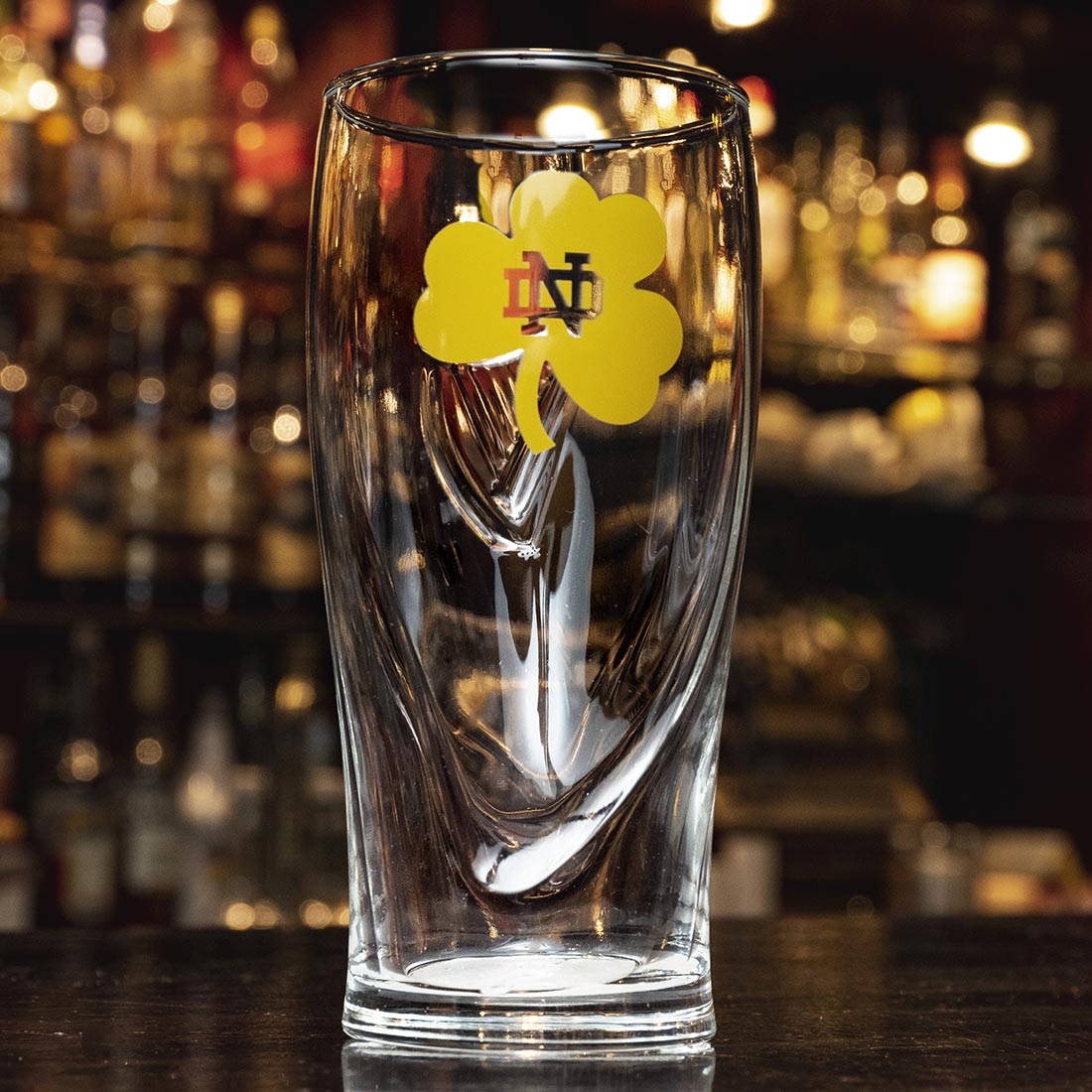 A Guinness pint glass sits on a bar with a shamrock on it.