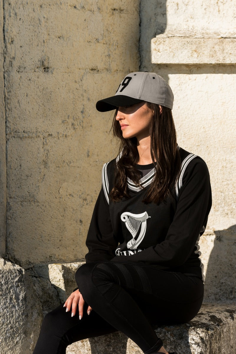 A woman sitting on a stone wall wearing the Guinness Grey 59 Baseball Cap (Adjustable).