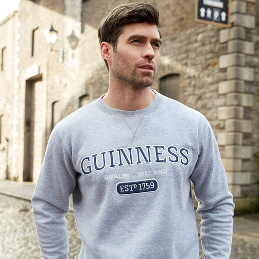 In Dublin, Ireland, a man proudly dons a unisex Guinness Grey Crew Neck Sweatshirt as he stands on a cobblestone street.