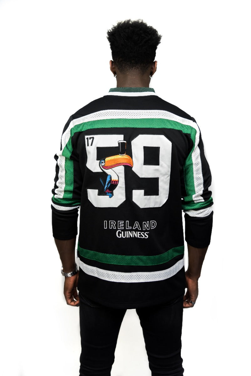 A person faces away, wearing the Guinness Toucan Hockey Jersey in black and green by Guinness, featuring the number 59, a toucan graphic, and "Ireland Guinness" on the back to honor Arthur Guinness's legacy.