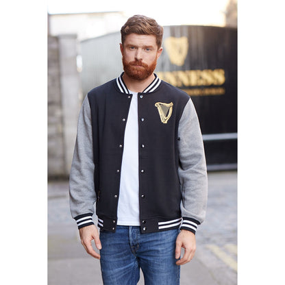 A man wearing a black and gold Guinness Letterman Jacket promoting merchandise.