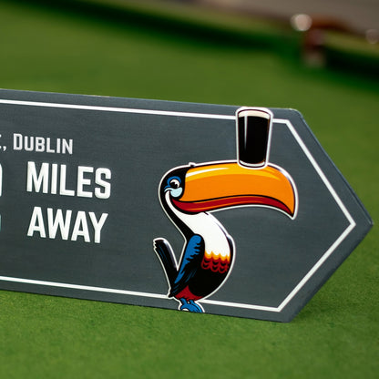 A Guinness Open Gate Brewery Arrow Metal Sign featuring a toucan with a hat on it, promoting Guinness and the Open Gate Brewery.