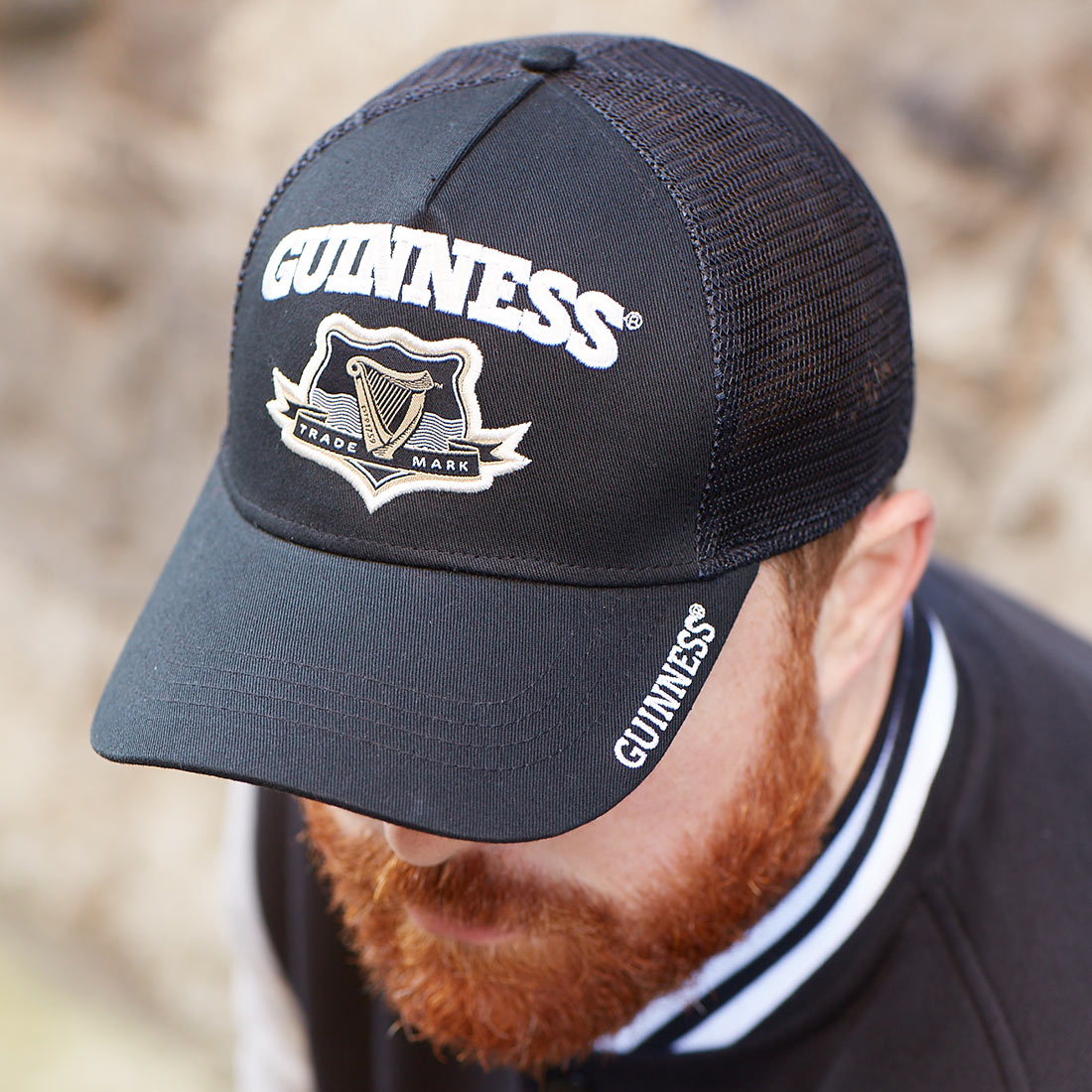 A bearded man sporting a Guinness Signature Black Trucker Mesh Baseball Cap Adjustable trucker hat.