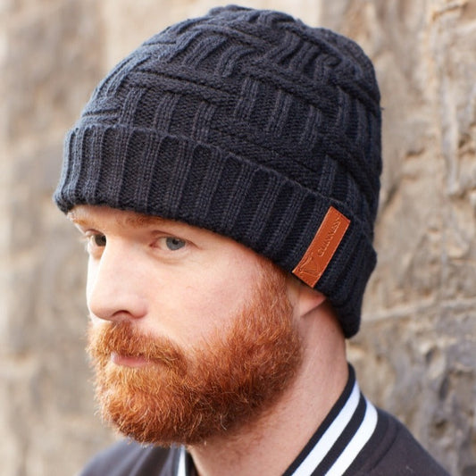 A man with a beard wearing a super warm Guinness Black Leather Patch Beanie made of soft yarn.