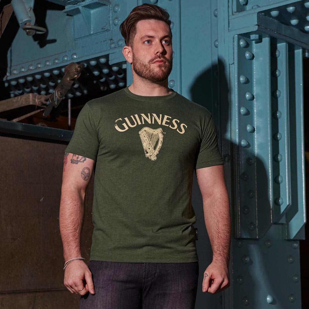 A man wearing a green Guinness Vintage Harp Tee featuring the Guinness logo.