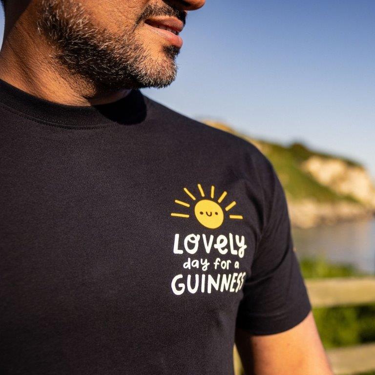 A man wearing a FATTI BURKE "LOVELY DAY FOR A GUINNESS" BLACK TEE, perfect for summer.
