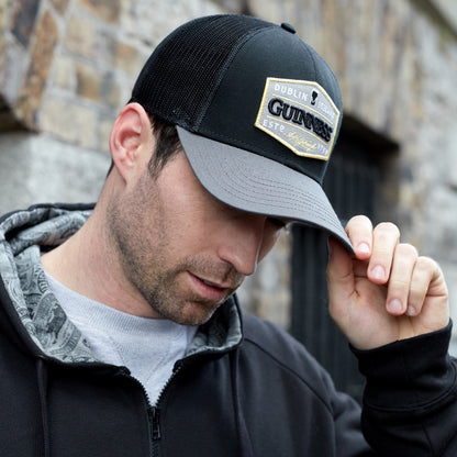 A man sporting an embroidered Guinness Trucker Premium Grey with Embroidered Patch Cap made of cotton.