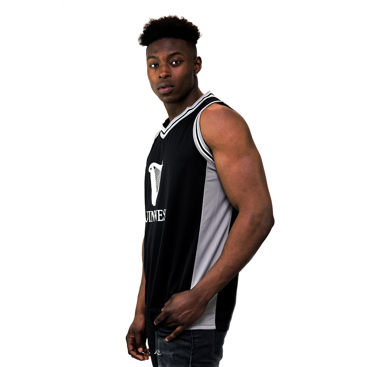Wearing the Guinness Black & Grey Basketball Jersey from Guinness Webstore US, a person stands confidently against a stark white background.