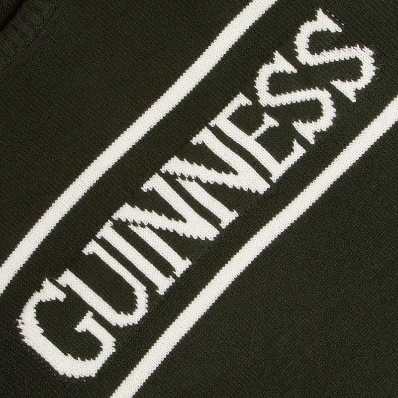 A close-up of the dark green Guinness Bottle Green Crew Neck Jumper by Guinness Webstore US shows the word "GUINNESS" in bold white letters, centered between two white horizontal lines, perfectly complementing the iconic Guinness Harp logo on 100% cotton fabric.