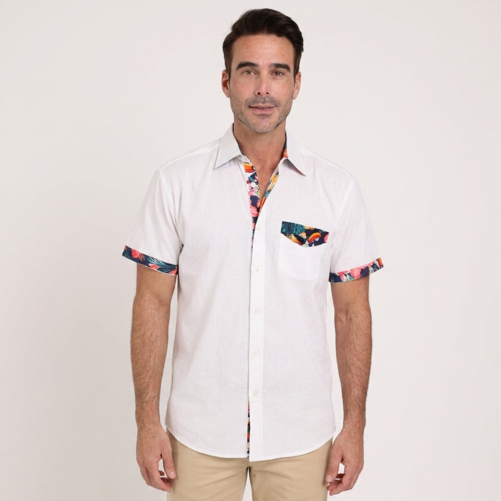 A man wears the Guinness Webstore US Guinness White Linen Summer Shirt with floral trim on the collar, pocket, and sleeves, paired with beige pants, standing against a plain light background.