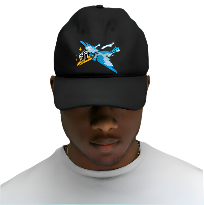 A man in a white t-shirt wears the Guinness Seb Curi Lovely Day Cap - Black from Guinness Webstore US, featuring Sebastian Curi’s embroidered blue bird and camera design, standing against a plain gray background.