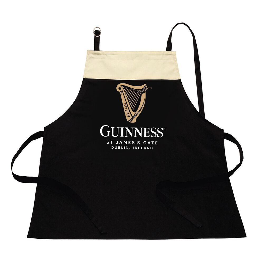 The Guinness Pint Apron, crafted from 100% cotton, showcases a black and beige design with the iconic Guinness harp logo. It features the text "Guinness, St James's Gate, Dublin, Ireland," making it an ideal accessory for handling kitchen spills with both ease and style.