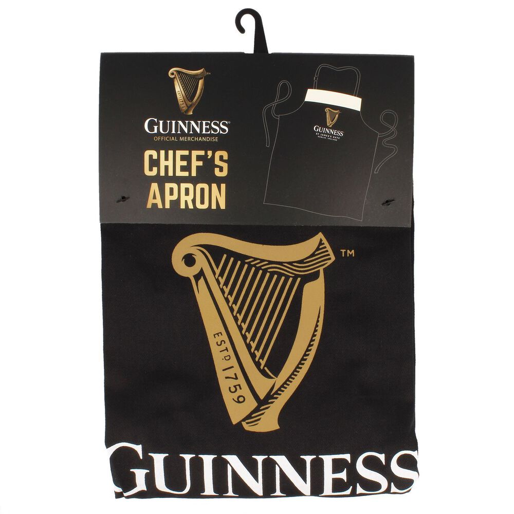 Guinness Pint Apron, a black apron featuring a gold harp design and "Guinness Estd 1759" text, is made from 100% cotton to manage kitchen spills effectively. It comes with labels that say "Chef's Apron" and belongs to the official Guinness merchandise collection.