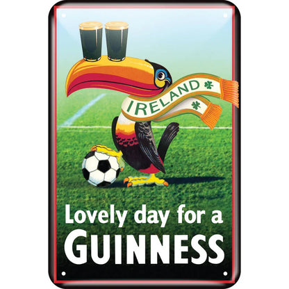 The Guinness Metal Sign - Toucan Ireland Football Scarf from the Guinness Webstore US features an illustration of a toucan balancing two pints of Guinness on its beak while wearing an "Ireland" scarf. Set against a vibrant soccer field with a ball nearby, this scene evokes vintage nostalgia, complemented by the text "My Goodness My Guinness.