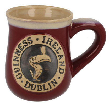 A Guinness Toucan Burgundy Pottery Mug from Guinness Webstore US with a beige handle featuring a Guinness Dublin Ireland logo with a toucan inside a circular emblem.