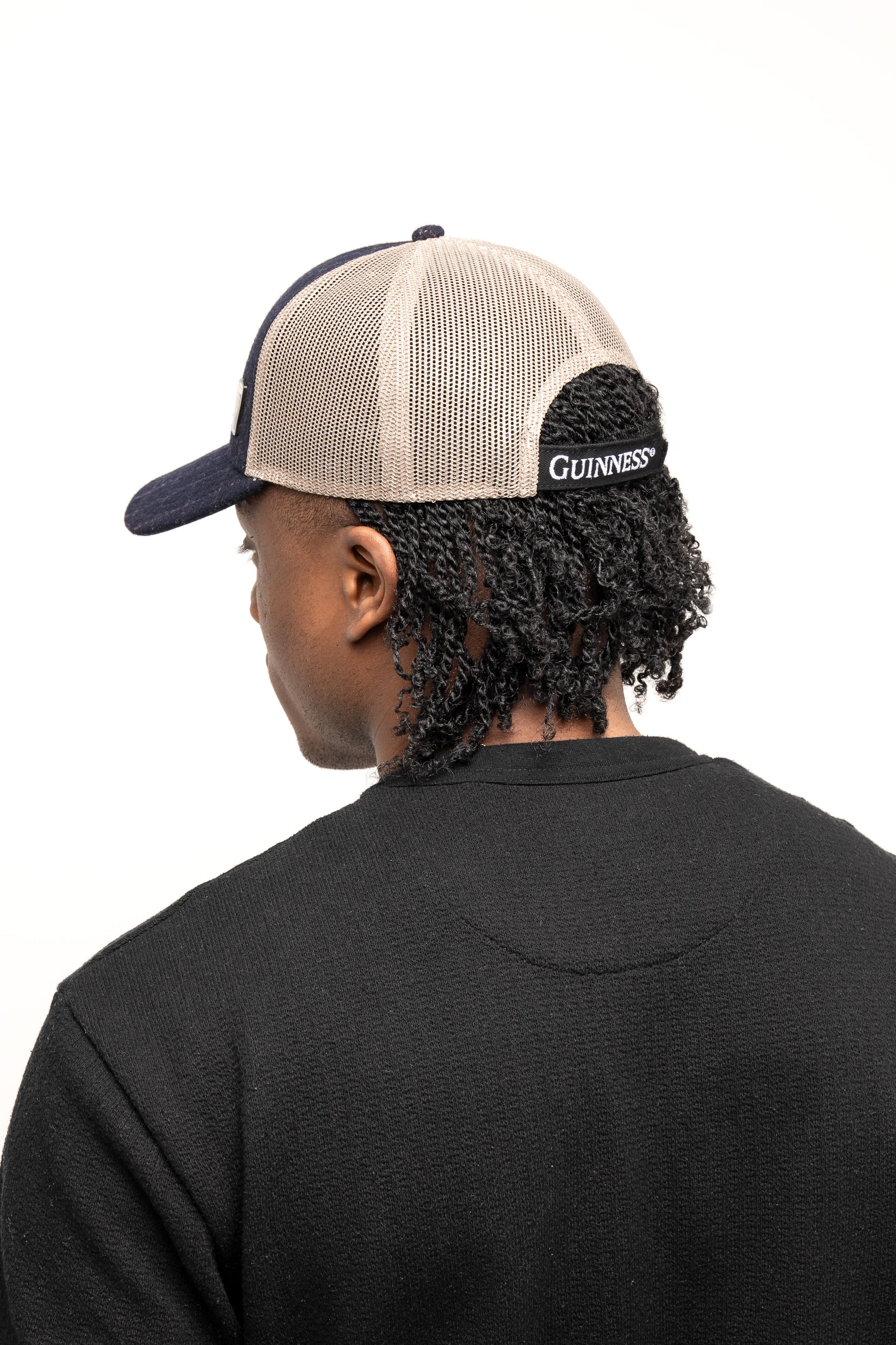 A person in a black shirt wears the Guinness Checked Trucker Cap by Guinness Webstore US, shown from behind and set against a plain background.