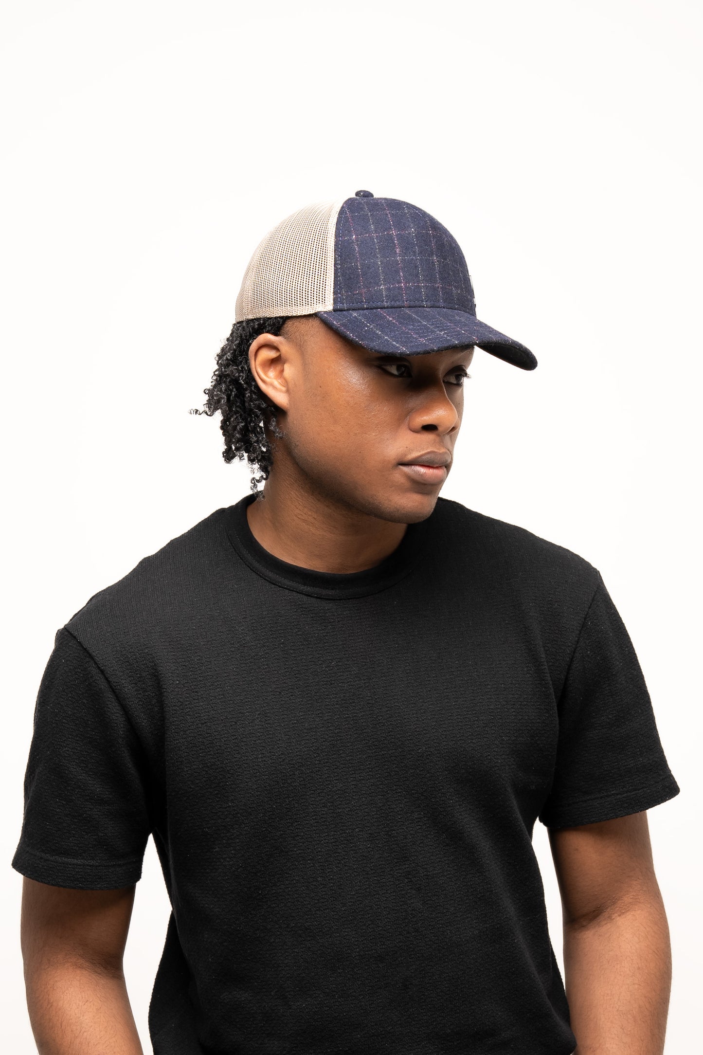 Person wearing a black t-shirt and a denim-textured navy Guinness Checked Trucker Cap from Guinness Webstore US with mesh back, looking slightly to the side against a plain white background.