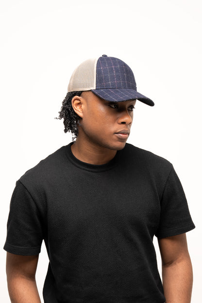 Person wearing a black t-shirt and a denim-textured navy Guinness Checked Trucker Cap from Guinness Webstore US with mesh back, looking slightly to the side against a plain white background.