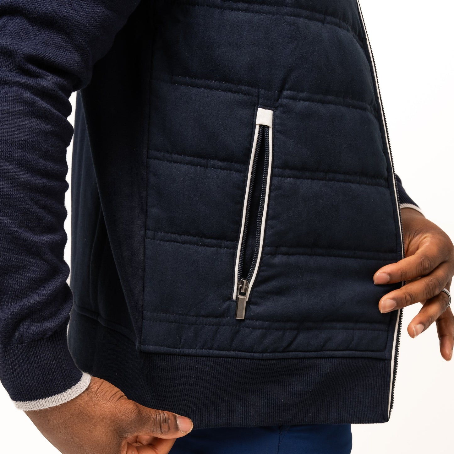 A person wears the navy Guinness Performance Gilet from Guinness Webstore US, featuring quilted detailing and blue shorts, with one hand near the gilet's zipper pocket and the other resting at their side.