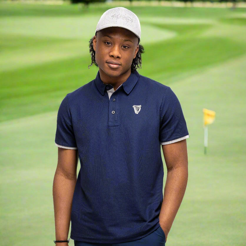 A person in a Guinness Performance Polo - Navy from Guinness Webstore US and a light cap stands on a golf course near a hole with a yellow flag.