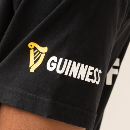 Close-up of a black Guinness Seb Curi Oversize Tee sleeve with a yellow harp logo and “GUINNESS” in white, from Guinness Webstore US and designed with Sebastian Curi.
