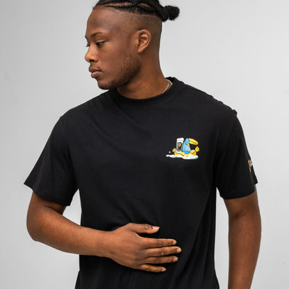 A man wearing the Guinness Seb Curi Oversize Tee - Black from Guinness Webstore US, featuring a small cartoon graphic, stands against a plain background looking left with one hand on his stomach.