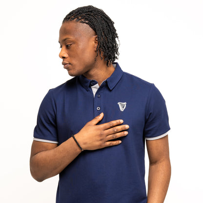 A man in a navy Guinness Performance Polo from Guinness Webstore US with a small embroidered logo looks left, his right hand on his chest.