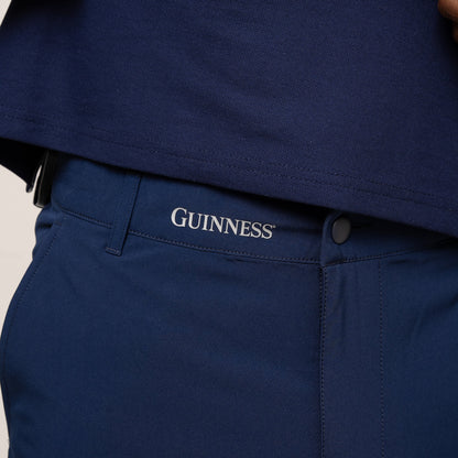 A person lifts a navy shirt, revealing Guinness Performance Shorts - Navy from Guinness Webstore US, featuring "GUINNESS" embroidered above the waistband and crafted from moisture-wicking fabric for all-day comfort.