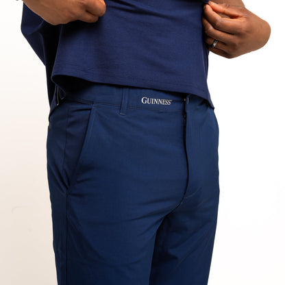 A person wearing a blue polo and pants with a "Guinness" logo waistband, lifts their shirt to show Guinness Performance Shorts - Navy by Guinness Webstore US, crafted from moisture-wicking fabric.