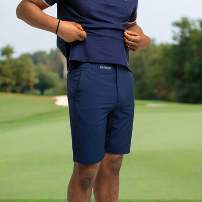 A person wearing Guinness Performance Shorts - Navy from Guinness Webstore US and a matching polo stands against a white background, lifting the shirt hem with both hands.