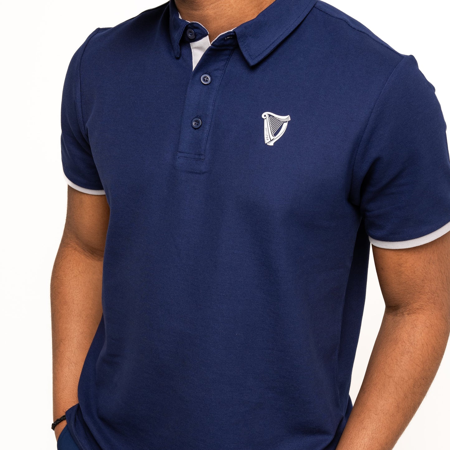 A person wearing the Guinness Performance Polo - Navy by Guinness Webstore US, featuring a white embroidered harp logo on the left chest, stands against a white background.