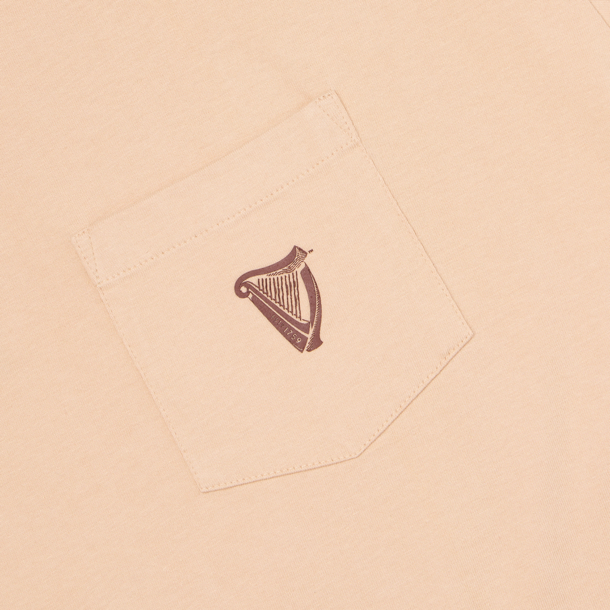 The Guinness Cooperage Ivory Heavyweight Tee features a beige fabric breast pocket with a small dark brown harp logo and “ESTD 1759” text.