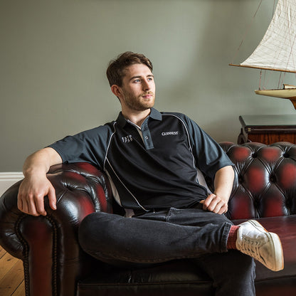 A man sitting on a leather couch wearing a Guinness Performance Golf Shirt.