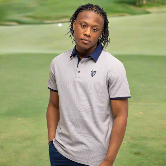A person stands against a white background wearing the Guinness Performance Polo - Grey from Guinness Webstore US with a dark collar and navy shorts, one hand in their pocket—perfect for stylish golf apparel seekers.