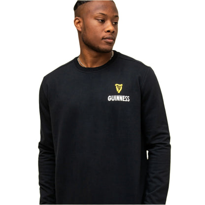 A man stands against a plain white background wearing the Guinness Seb Curi Lovely Day Sweatshirt - Black from Guinness Webstore US, featuring a small yellow logo on the left chest.