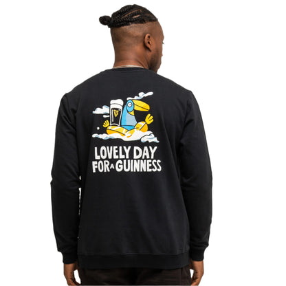 Person facing away, wearing the Guinness Seb Curi Lovely Day Sweatshirt in black from Guinness Webstore US, featuring Sebastian Curi’s artwork—a toucan, pint of Guinness, clouds, and "Lovely Day For A Guinness" text on the back.