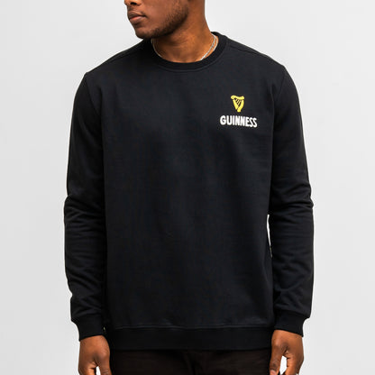 A man stands against a plain white background wearing the Guinness Seb Curi Lovely Day Sweatshirt in black from Guinness Webstore US, featuring a small logo and text on the left chest.