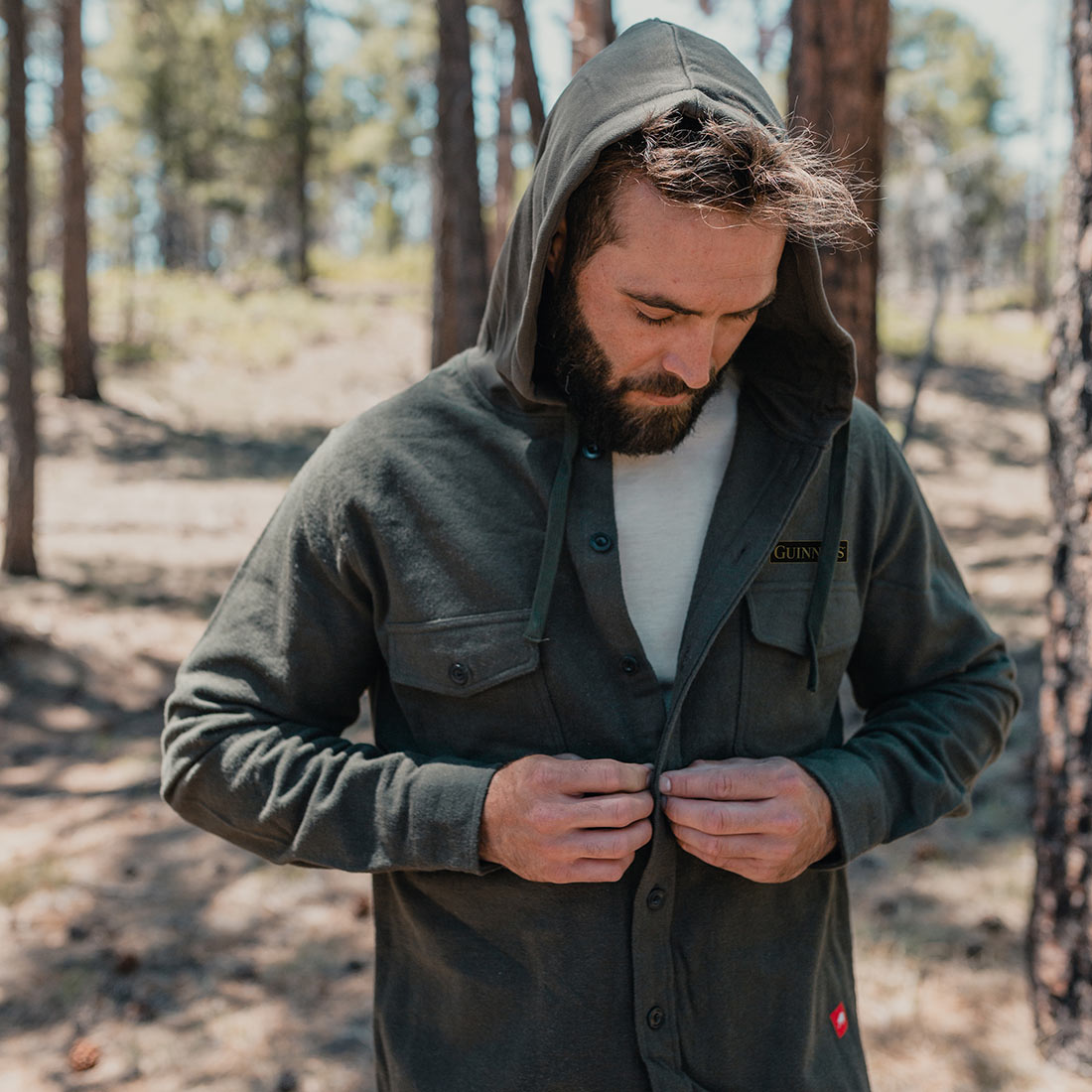 A man wearing a Guinness Deep Green Shirt Jacket and hoodie in the woods.